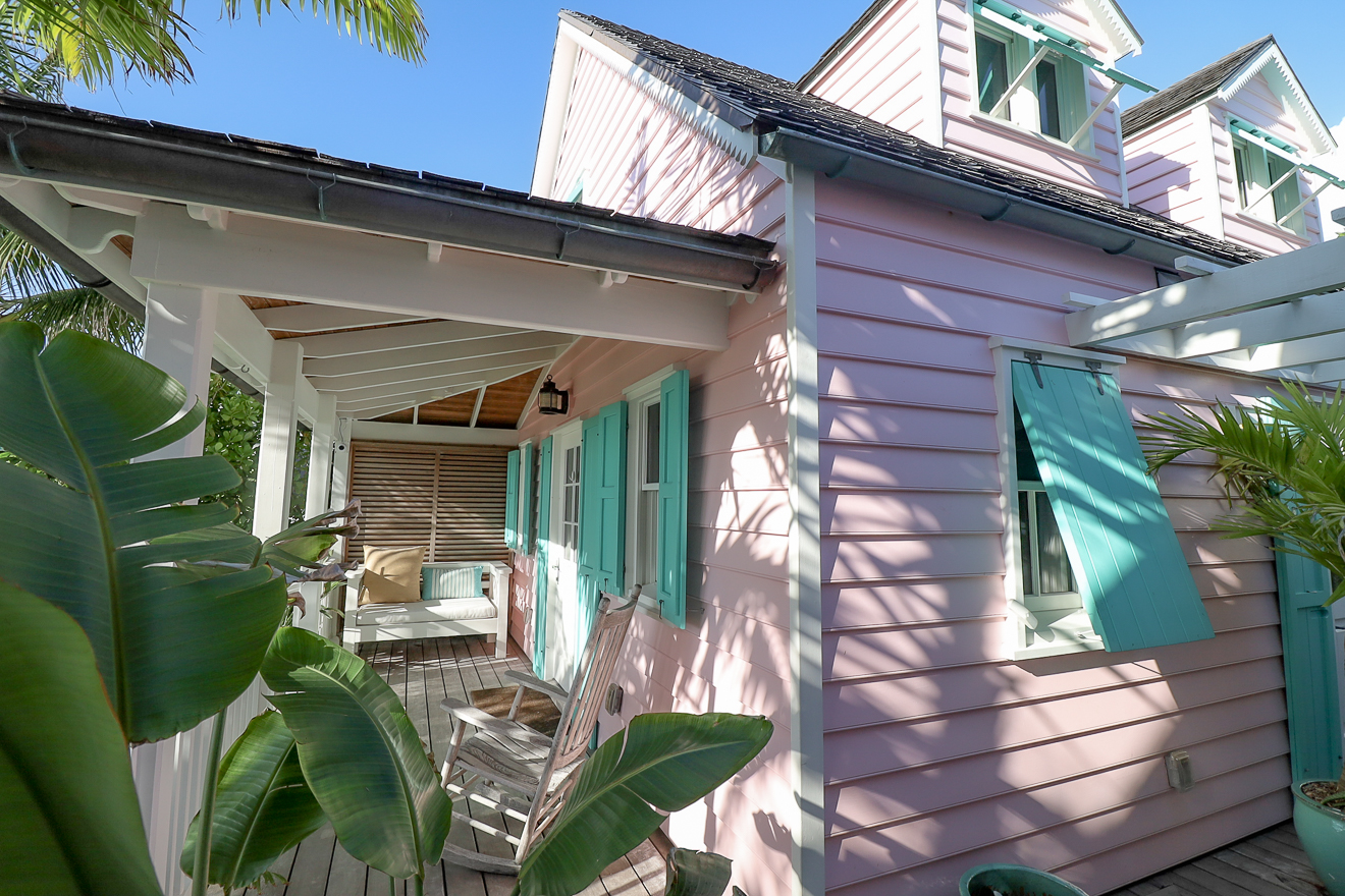 Front porch of pink cottage with outdoor seating and teal-shuttered windows